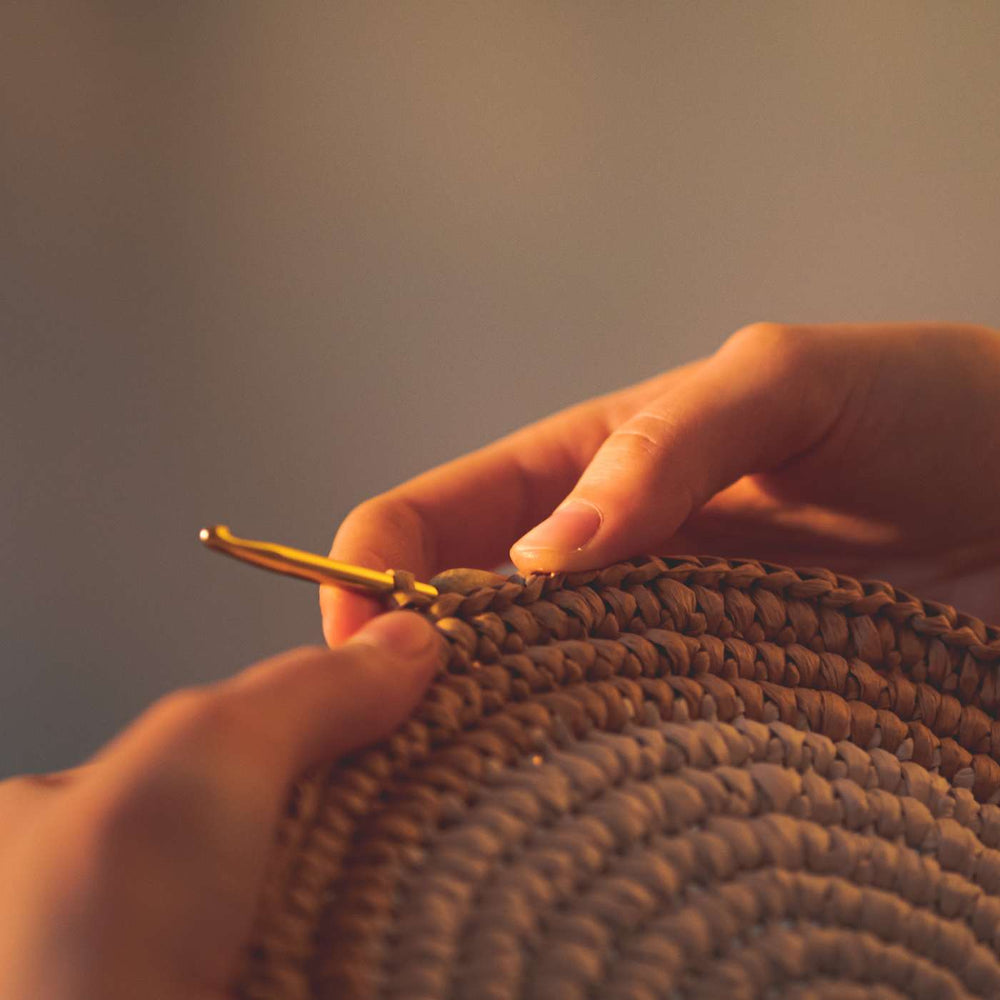 two hands crocheting the base of a basket using raffia