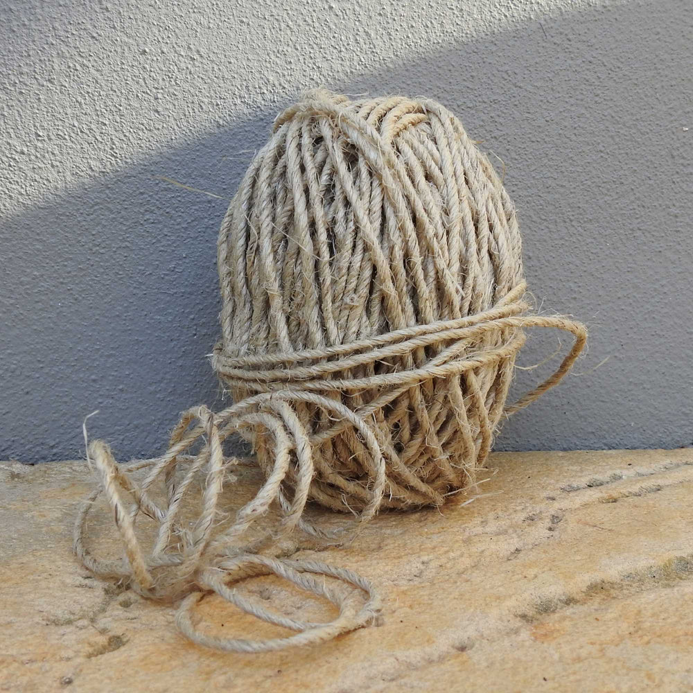 ball of thick and chunky natural hemp yarn sitting next to a wall. a rustic yarn for weaving, baskets, garden. also available in charcoal